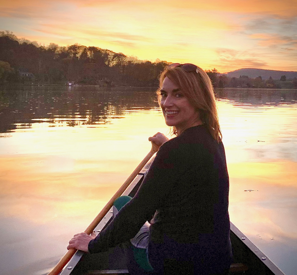 christine bosco padding a canoe on water at sunset