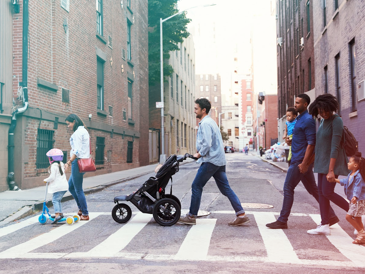Two families are crossing the street with a stroller and scooter.